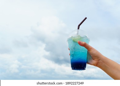 Close Up Hand Holding Glass Of Blue Hawaii Drink With Ice Over Sky Background.