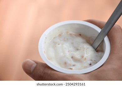 Close up a hand holding a glass of yogurt with Cereal cornflakes for breakfast on brown blurred background. Yogurt and cornflakes, Whole Grain, Granola, Muesli on a cup and spoon. - Powered by Shutterstock