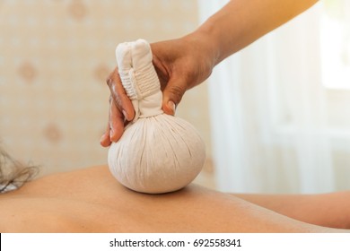 Close up of hand holding herbal compress ball in Thai spa. Thai Ball Massage. Back plate woman getting thai herbal compress massage.