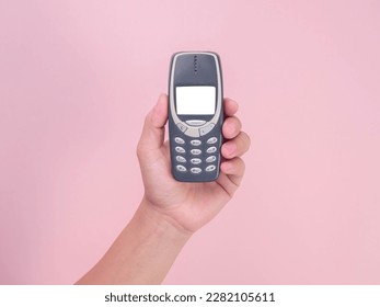 Close up hand holding mobile phone Nokia 3310 isolated on pink background. Female hand holding old used phone Nokia 3310.