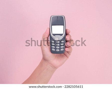 Close up hand holding mobile phone Nokia 3310 isolated on pink background. Female hand holding old used phone Nokia 3310.