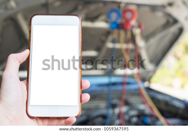 Close up hand holding mobile smartphone white\
screen with copy space for text in front of mechanic repairing car\
using Manifolds Gauge air conditioning in auto vehicle fill\
refrigerant in car\
garage.