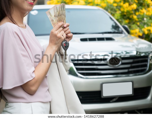 Close up of hand holding money and
car key against a car. insurance, loan and finance
concept