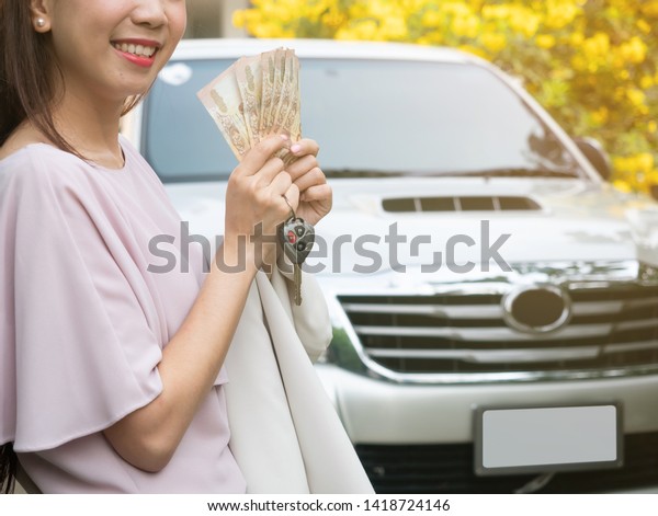 Close up of hand holding money and\
car key against a car. insurance, loan and finance\
concept