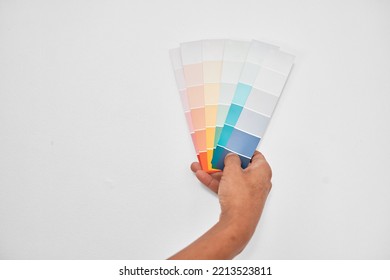 Close Up Of A Hand Holding Pastel Coloured Paint Swatches Against Pale Grey Wall