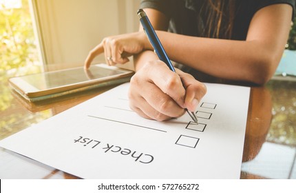 Close- Up Hand Holding Pen On Check List Paper With Tablet In Vintage Style