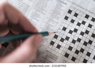 Close up hand holding pencil over crossword puzzle on newspaper. Game on for writing some letters to solve and completing the empty table.