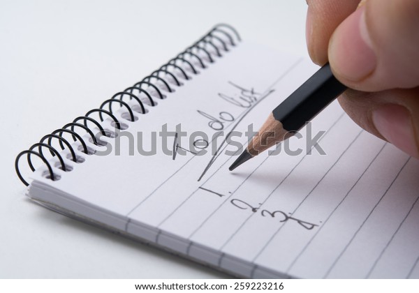 Close up of hand holding a pencil and writes the to\
do list. Isolated on\
white