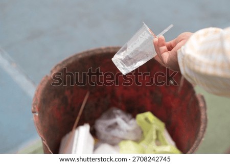 close up of a hand holding a plastic drinking cup in the trash