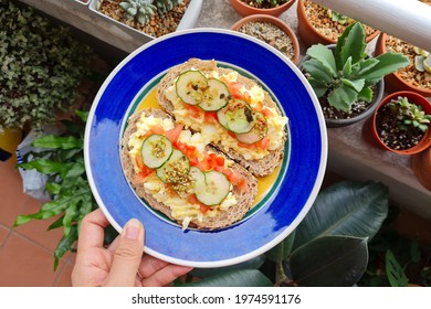 Close Up Hand Holding A Plate Of Fresh Healthy Sourdough Bread Sandwich With Egg Mayo Spread, Tomatoes And Cucumber.