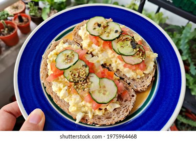 Close Up Hand Holding A Plate Of Fresh Healthy Sourdough Bread Sandwich With Egg Mayo Spread, Tomatoes And Cucumber.