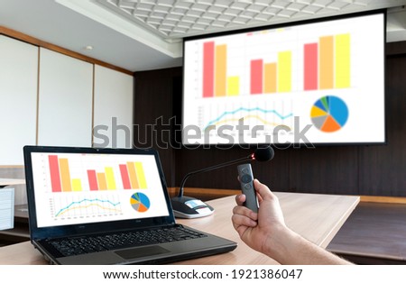Close up hand holding a remote control slide presentation with presentation meeting on laptop and srceen in meeting room.