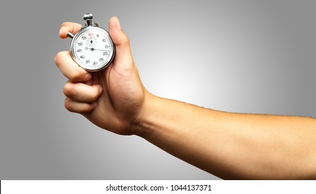 Close Up Of Hand Holding Stopwatch against a grey background - Shutterstock ID 1044137371