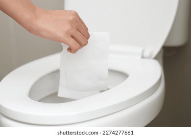 close up hand holding a tissue to be thrown into the toilet bowl. Can not drain water of toilet paper in the toilet bowl cause the stool to clog up.