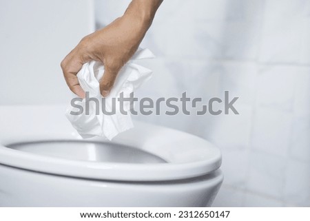 close up hand holding a tissue to be thrown into the toilet bowl. Can not drain water of toilet paper in the toilet bowl cause the stool to clog up.