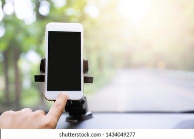 Close Up Hand Holding Using Mobile Smart Phone With Black Screen In Car Console Front Windshield Holder Stick. Insert Map Gps Navigation Travel On The In The Background Of The Dashboard. Copy Space. 