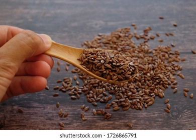 Close up hand holding the wooden spoon with brown Flax seeds or Linseeds or Common flax on wooden table background. Flax seeds are rich of omega fat. Top view.