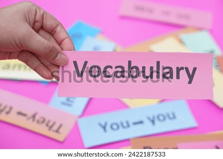 Close up hand holds paper card with text vocabulary. Concept, education, learning, studying language. Education. Reading and memorizing strategy of learning process lesson.