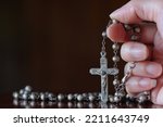 Close up of hand with the holy rosary to pray isolated on black background. Beautiful Roman Catholic item, rosary made from silver in rose pattern. Life of faith concept.

