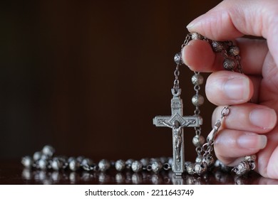 Close up of hand with the holy rosary to pray isolated on black background. Beautiful Roman Catholic item, rosary made from silver in rose pattern. Life of faith concept.

