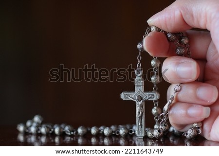 Close up of hand with the holy rosary to pray isolated on black background. Beautiful Roman Catholic item, rosary made from silver in rose pattern. Life of faith concept.

