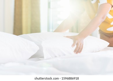 Close up hand of housekeeper set up white pillow on the bed sheet in hotel room at morning time with sunlight from windows - Shutterstock ID 1596886918
