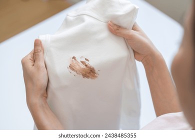 Close up hand of housewife, maid woman holding white t-shirt, showing making cloth stain, spot dirty or smudge on clothes, dirt stains for cleaning before washing, making household working at home. - Powered by Shutterstock