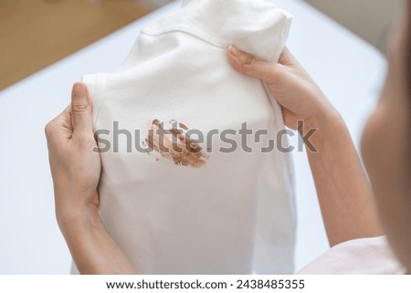 Close up hand of housewife, maid woman holding white t-shirt, showing making cloth stain, spot dirty or smudge on clothes, dirt stains for cleaning before washing, making household working at home.