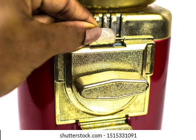 Close Up Of A Hand Inserting A 25 Cent USD Quarter Into The Knob Turning Mechanism Of A Coin Operated Red & Gold Candy Gumball Vending Machine