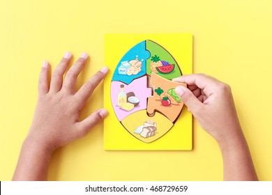 Close up hand of kid holding wooden jigsaw of the 5 food Groups. Child development concept