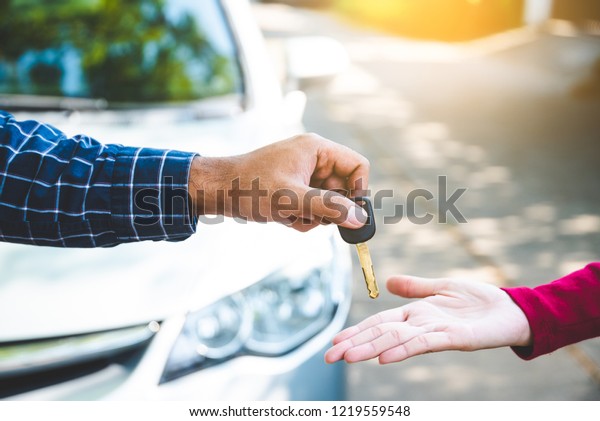 Close up hand male
giving a key new car on hand female outside her car. Concept of
rent car or buying car. 