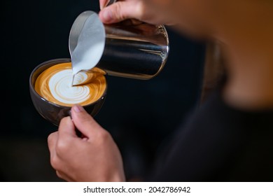 Close up hand of man barista pouring froth milk in espresso coffee in coffee cup making caffe latte art serve to customer. Small business cafe and restaurant owner and part time job working concept