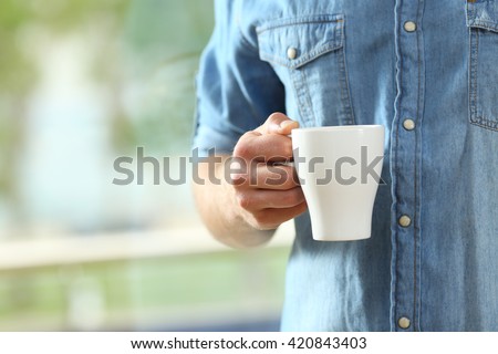 Close up of a hand of man holding a coffee cup beside a window with a green background outside