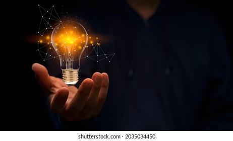 Close up hand of man holding illuminated light bulb in black background. idea, innovation, thinking, and inspiration for business concepts. Cyber digital data idea. - Shutterstock ID 2035034450