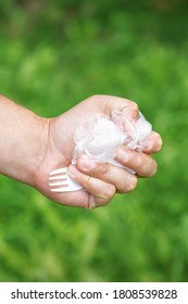 Close Up Of Hand Of Man Holding Plastic Utensils Trash On A Background Of Green Grass In The Park