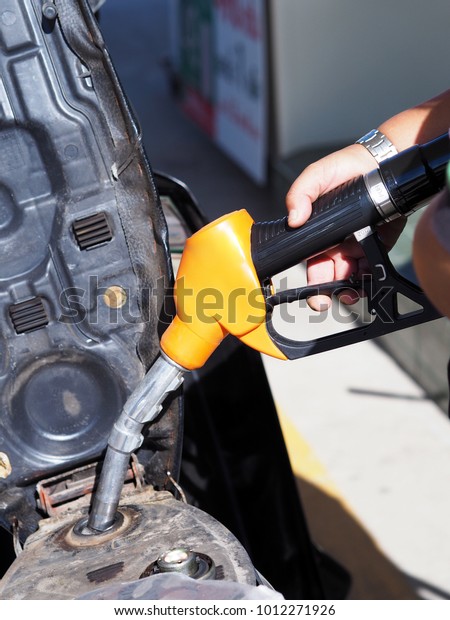 Close up hand of man pumping gasoline fuel in\
motorcycle car at gas\
station.