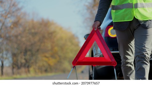 Close up hand of man putting warning triangle by the broken car on a road. Concept road accident. Help repair. - Shutterstock ID 2073977657