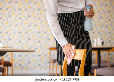 Close Up Hand Of Man Wipe Cleaning Wooden Chair With Spray Alcohol For Sterilize In Restaurant. Employee Cleaning At Workplace.