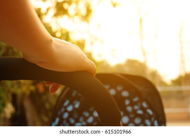 Close Up Hand Mom Pushing Stroller In The Park With Sunset.