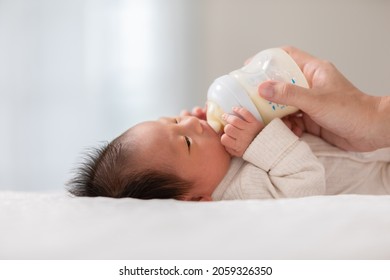 Close up hand of mother holding milk bottle Newborn baby lying on bed drinking milk.Cute infant baby feeding milk with love at home.Newborn Baby Concept