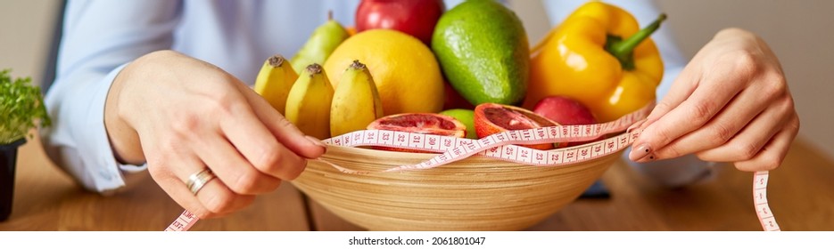 Close up of hand Nutritionist, dietitian workplace, woman hold measuring tape and measuring bowl with healthy vegetables and fruits, healthcare and diet, right nutrition and slimming wellness concept.