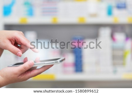 Close up hand Pharmacist using mobile smart phone for search bar on display in pharmacy drugstore shelves background.Online medical concept.