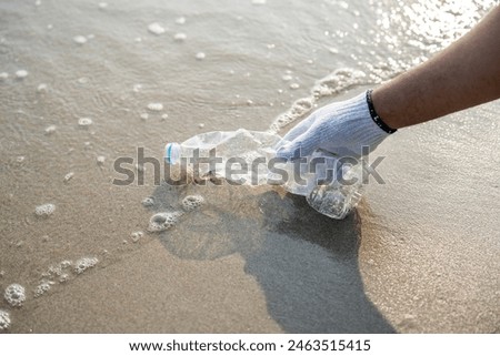 Close up hand pick up the plastic bottle on the beach. People male and female Volunteer with garbage bags clean the trash on the beach make the sea beautiful. World environment day Ecology CSR.