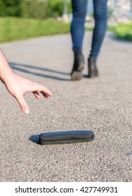 Close up of a hand picking a lost wallet from ground while owner walks away