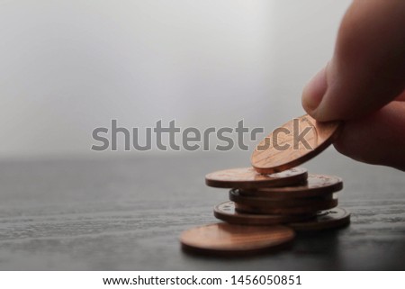 Close up of a hand placing a penny on top of a stack of pennies on a black wooden surface. Savings concept