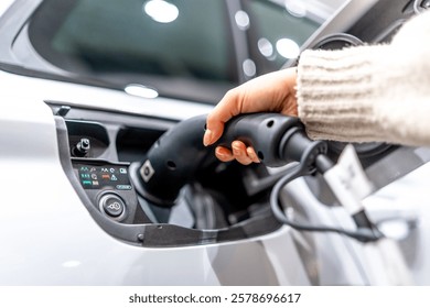 Close up of a hand plugging a charging cable into an electric vehicle at a car dealership, showcasing the transition to sustainable transportation