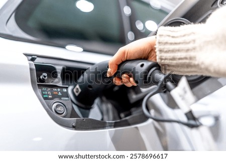Close up of a hand plugging a charging cable into an electric vehicle at a car dealership, showcasing the transition to sustainable transportation