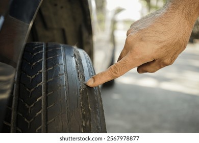 close up of hand points at an old worn tire with bald tread. Deteriorated tires have damage to the tread. Concept of car maintenance and dangers from old and worn tires from use