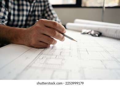 close up of hand professional architect, engineer or interior reviewing blueprint on workplace desk in office center at construction site, contractor, construction, engineering and business concept - Powered by Shutterstock