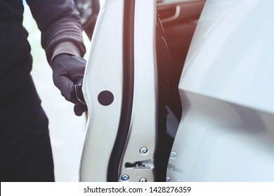 Close up hand pulling the handle of a car thief  wearing black clothes and glove stealing automobile trying door handle to see if vehicle is unlocked  trying to break into. car theft concept.